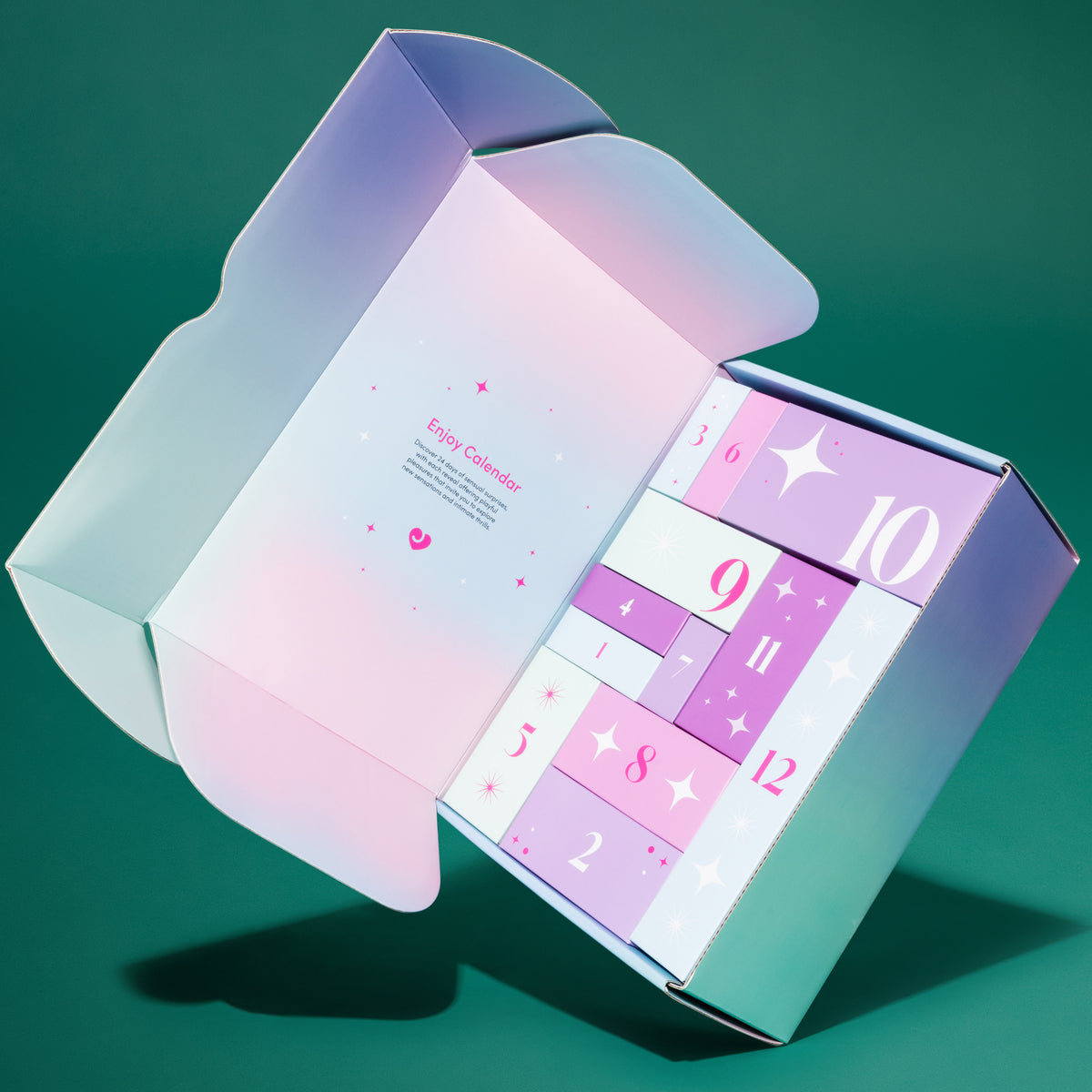 An open pastel gradient gift box with a colorful numbered advent calendar insert inside, photographed on a teal-green studio background.