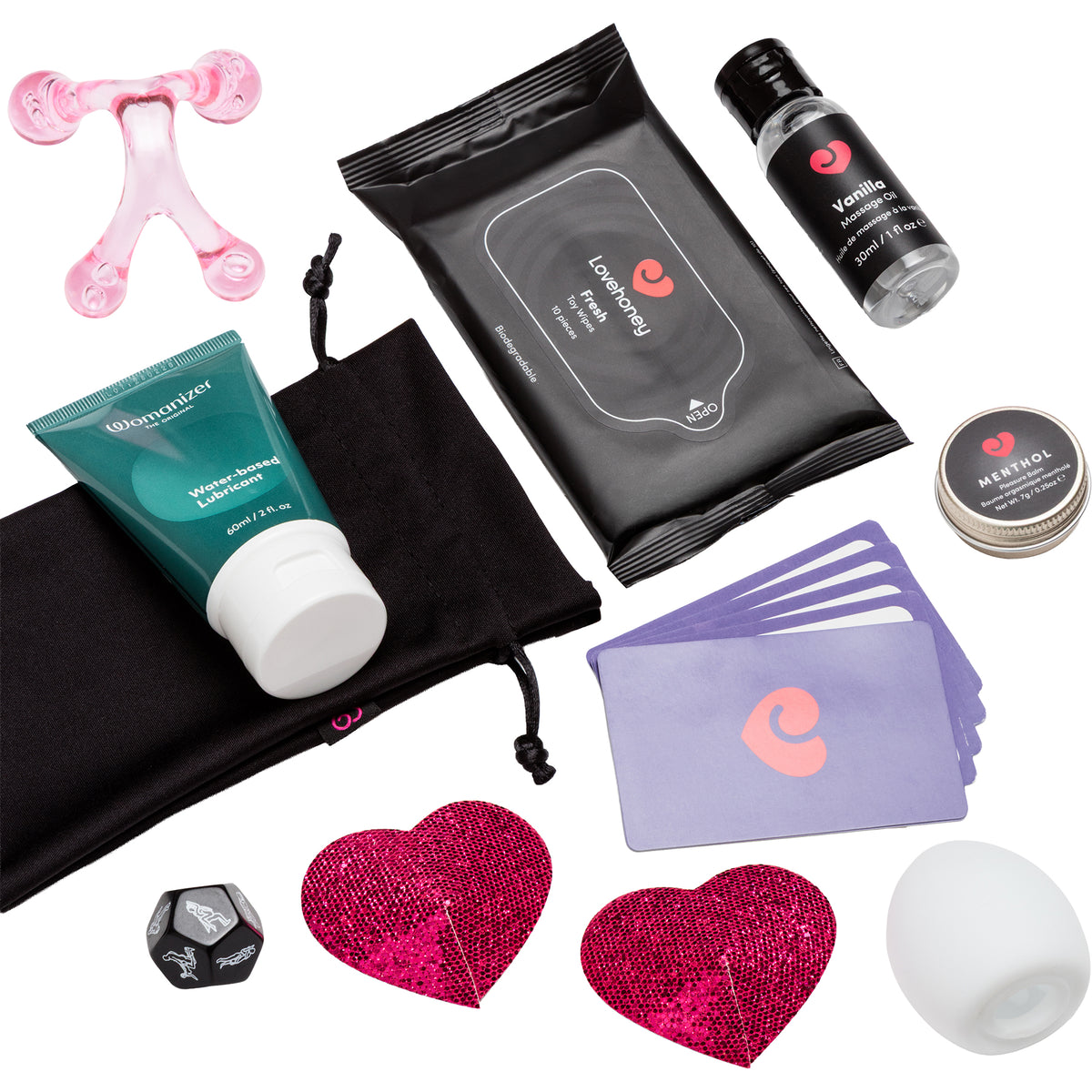 A wellness gift set arranged on a white background, including a pink silicone baby teether, a black pouch of Lovehoney wipes, a teal tube of Water-Based Lubricant, a small black bottle of Vanilla Massage Oil, a round tin of Menthol Pleasure Balm, lavender cards, two pink sequined heart pasties, a black toy bag, and a white stroker.