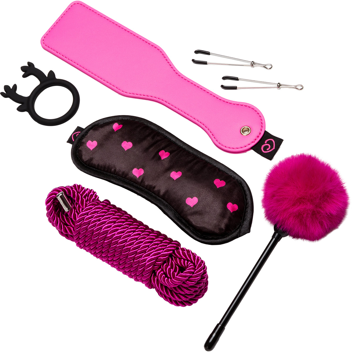 A pink and black adult novelty kit laid out on a white background, including a bright pink strap, a black satin blindfold with pink hearts, a coiled magenta rope, a fluffy hot pink pom-pom stick, three metal pins, and a black reindeer-shaped ring.