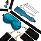 A multi-piece adult novelty gift set arranged on a white background, including a black harness with gold-tone hardware, a satin teal blindfold, a teal leather-like strap tool, several silver metal tools, and a small teal pouch.