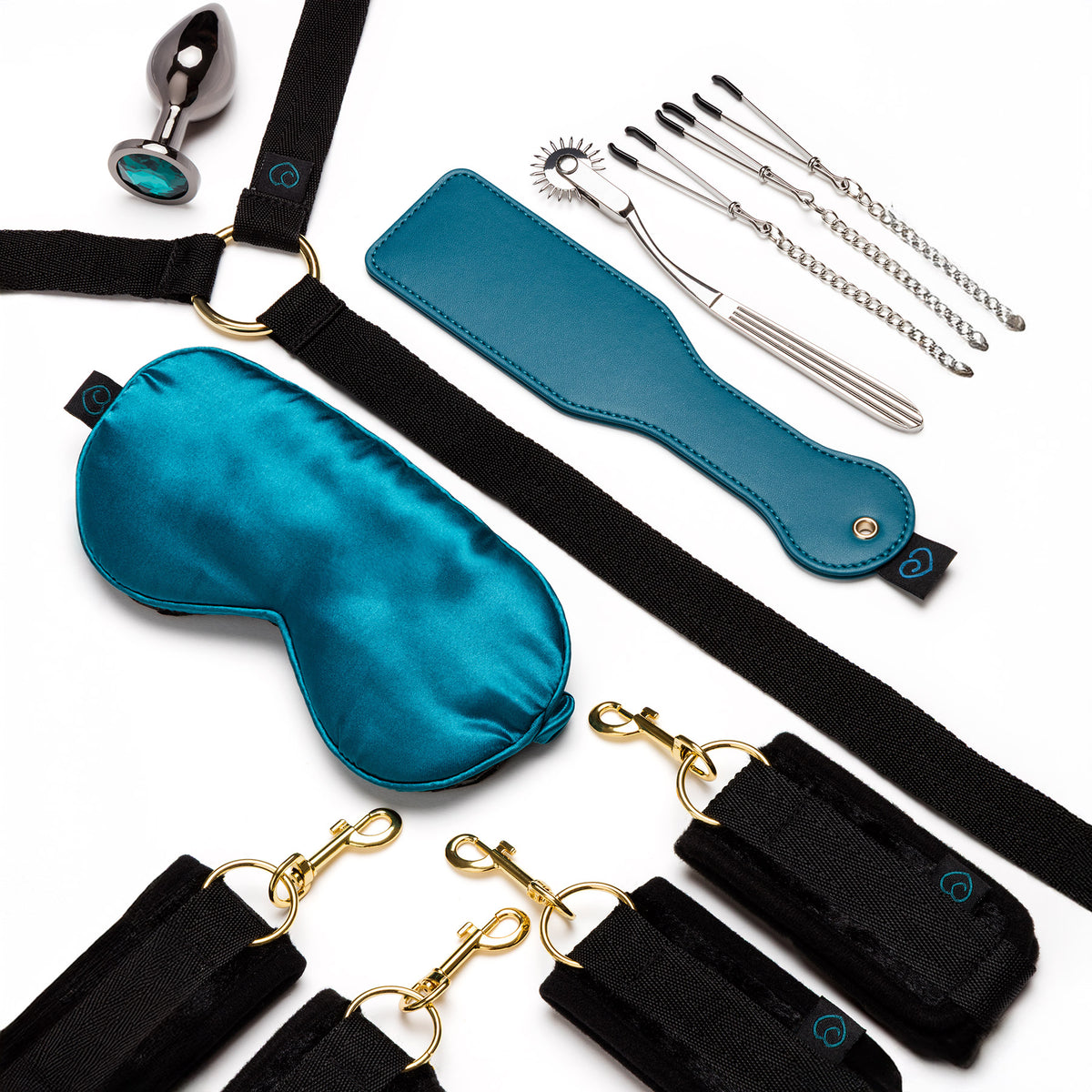 A multi-piece adult novelty gift set arranged on a white background, including a black harness with gold-tone hardware, a satin teal blindfold, a teal leather-like strap tool, several silver metal tools, and a small teal pouch.